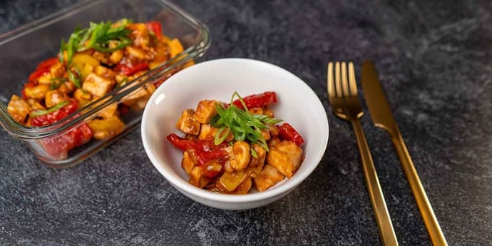 Paleo Cashew Chicken Recipe plated on a white bowl and meal prep container next to golden silverware