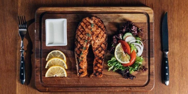 Paleo dish of grilled fish filet with a simple side salad plated on an oak cutting board