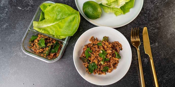 Paleo Thai Turkey Larb Recipe plated on a white bowl and glass meal prep container with a side of lettuce and lime next to golden silverware